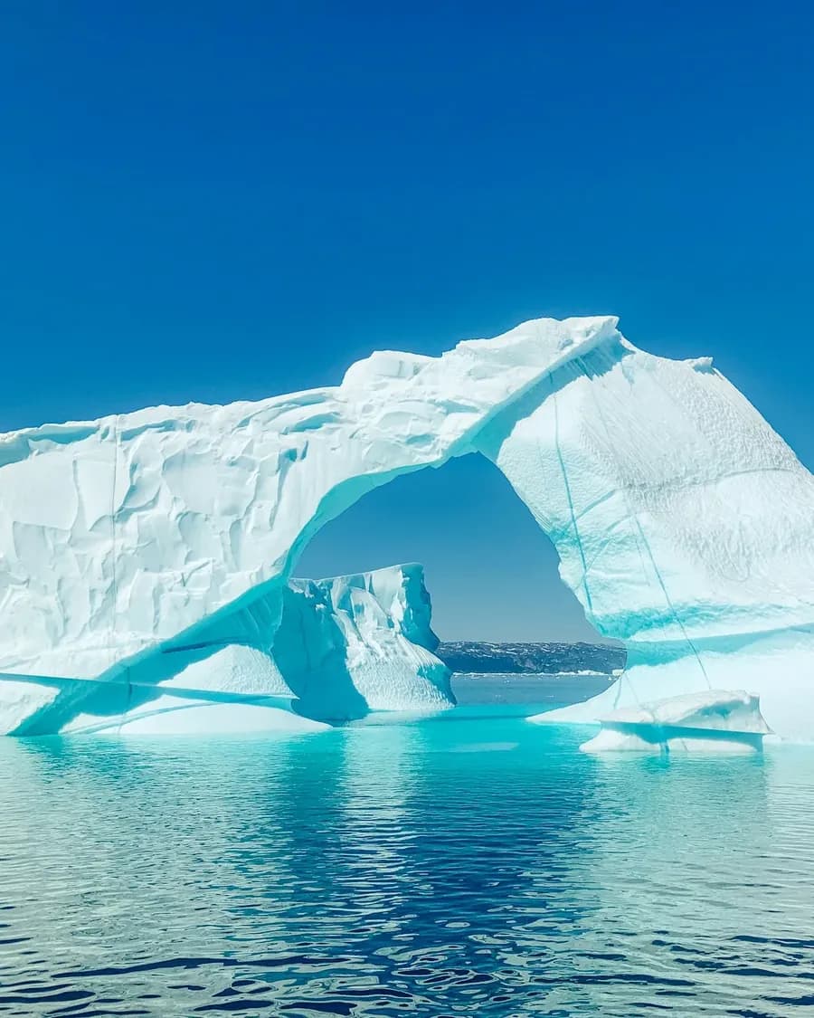 Eisbogen eines türkis leuchtenden Eisbergs im arktischen Meer