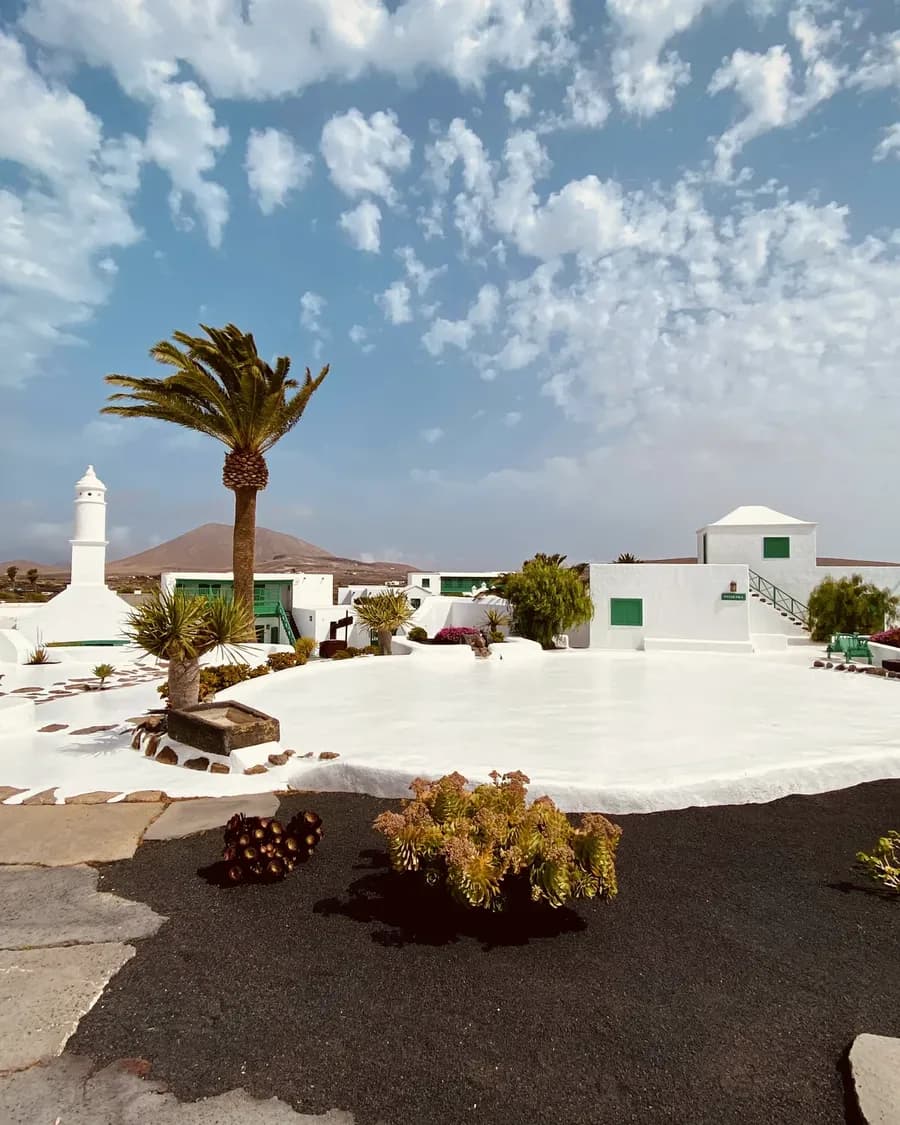 Weiß getünchtes Gehöft mit Palme vor einem Vulkankegel auf Lanzarote