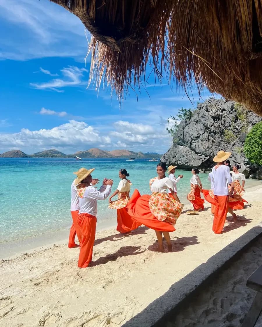 Tänzerinnen und Tänzer in traditioneller Tracht an einem Palmenstrand in der Südsee